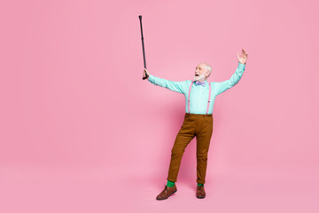 Full size photo of active crazy grandpa moving dance senior party raise up walk stick wear mint shirt suspenders bow tie pants shoes green socks isolated pink pastel background
