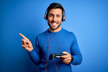 Young handsome gamer man with beard playing video game using joystick and headphones very happy...