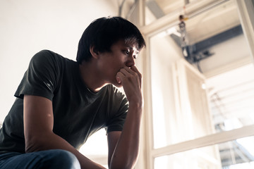 Fototapeta premium Asian male unemployed worker sitting on chair feeling stress and unhappy that have no job due to covid-19 virus cause him to be laid off. Man thinking how to find money in bad global economic crisis.
