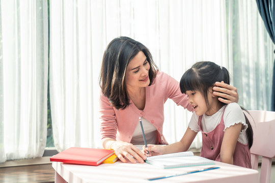 Homeschool Asian young little girl learning, reading and does homework with kind mother help, teach and encourage. Mom hug daughter and smile. Girl happy to study at home education together with mom.