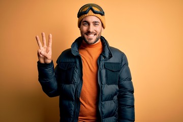 Young handsome skier man with beard wearing snow sportswear and ski goggles showing and pointing up...