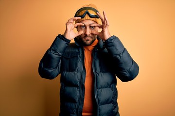 Young handsome skier man with beard wearing snow sportswear and ski goggles Trying to open eyes with fingers, sleepy and tired for morning fatigue