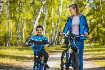 Fototapeta na wymiar Funny boy cyclistrides a bike with mom in the sunny forest on a bike. Adventure travel.