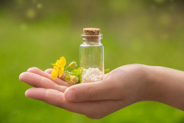 glass container with homeopathic granules and a flower in the palm of your hand. beautiful natural...