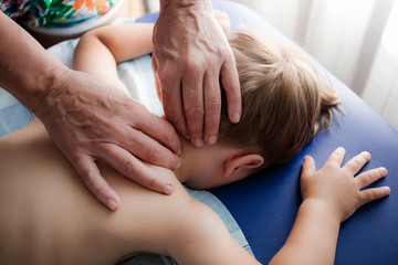 Doctor osteopath massage therapist is doing massage to a little boy. Hands massage the back and cervical-collar zone. Mom gives her baby a massage.
