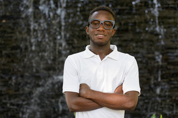 Portrait of happy young African nerd man smiling with arms crossed outdoors