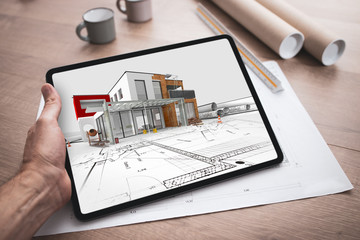 Tablette numérique tenue en main par un architecte qui travaille et réalise l'esquisse d'un...