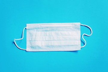 Disposable medical mask on a blue background. Deficiency of personal protective equipment during coronavirus