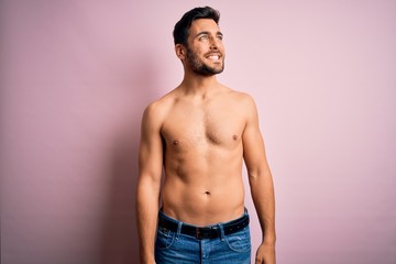 Young handsome strong man with beard shirtless standing over isolated pink background looking away to side with smile on face, natural expression. Laughing confident.