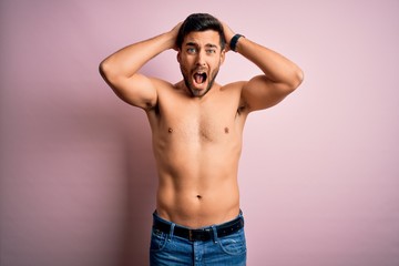 Fototapeta premium Young handsome strong man with beard shirtless standing over isolated pink background Crazy and scared with hands on head, afraid and surprised of shock with open mouth