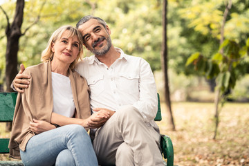 Fototapeta premium Caucasian senior elder couple sit on bench in park. Mature happy and enjoy with slow life. Old man hug and woman put head on his shoulder . They smile with life together. Retirement family lifestyle.