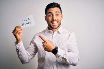 Young business man holding fake news paper over isolated background very happy pointing with hand...