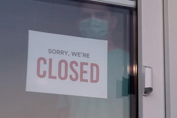 Business owner in medical mask puts a CLOSED sign