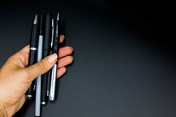 female hand holds and show four Traditional black and gray Pens isolated against a black background. Space for text, close up
