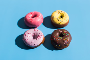 Colourful round donuts at bright blue background. Sweet donuts. Trendy sunlight Summer pattern Minimal summer concept.
