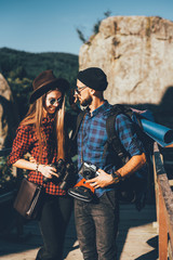 A couple traveling by the mountains wearing hipster clothes with backpack, vintage camera and binoculars. Toned photo