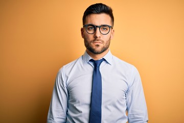 Young handsome businessman wearing tie and glasses standing over yellow background Relaxed with...