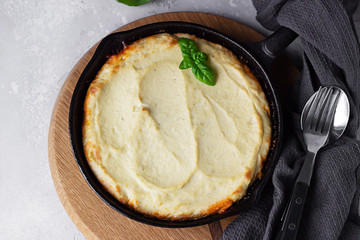 Shepherd's pie. Traditional British meal with minced meat, mashed potatoes and vegetables in cast iron pan. Autumn dinner, comfort food. Grey stone background, selective focus. Top view.