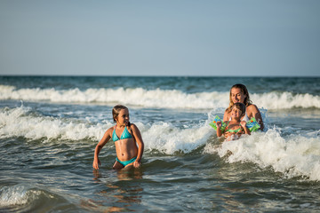 Obraz premium Cheerful young mother swims in the sea with her charming little daughters and enjoy the long-awaited weekend on a sunny summer day. Concept family vacation.