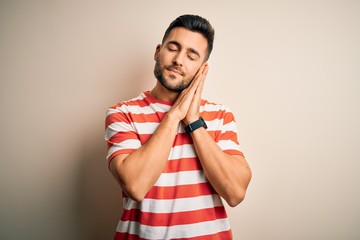Young handsome man wearing casual striped t-shirt standing over isolated white background sleeping tired dreaming and posing with hands together while smiling with closed eyes.