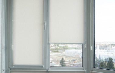 Details of white fabric roller blinds on the plastic window with wood texture in the living room.