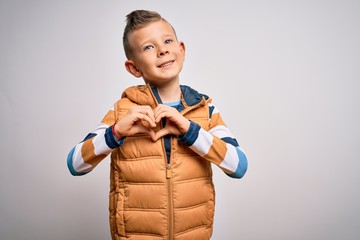 Young little caucasian kid with blue eyes standing wearing winter coat over isolated background smiling in love showing heart symbol and shape with hands. Romantic concept.