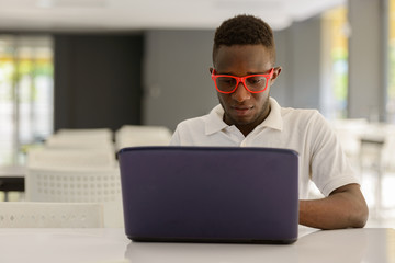 Young African man as student using laptop inside modern building