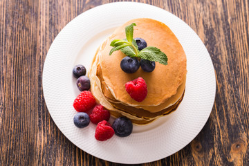 Homemade sweet pancakes with blueberries and raspberries on a white plate, top view.