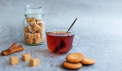 A Cup of fragrant tea on a gray table, with cane sugar, cookies, and cinnamon. Close-up, selective focus