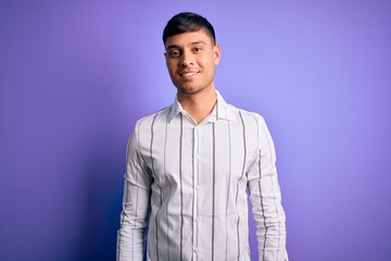 Young handsome hispanic man wearing elegant business shirt standing over purple background with a happy and cool smile on face. Lucky person.