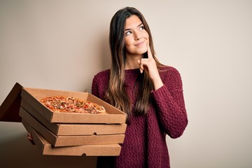 Young beautiful girl holding delivery boxes with Italian pizza standing over white background...