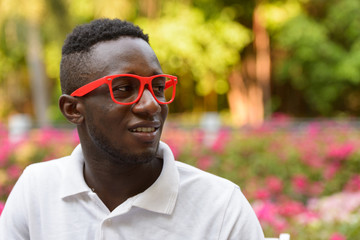 Naklejka na ściany i meble Face of happy young African man with eyeglasses thinking at the park outdoors
