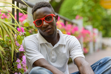 Young African man with eyeglasses sitting at the park outdoors