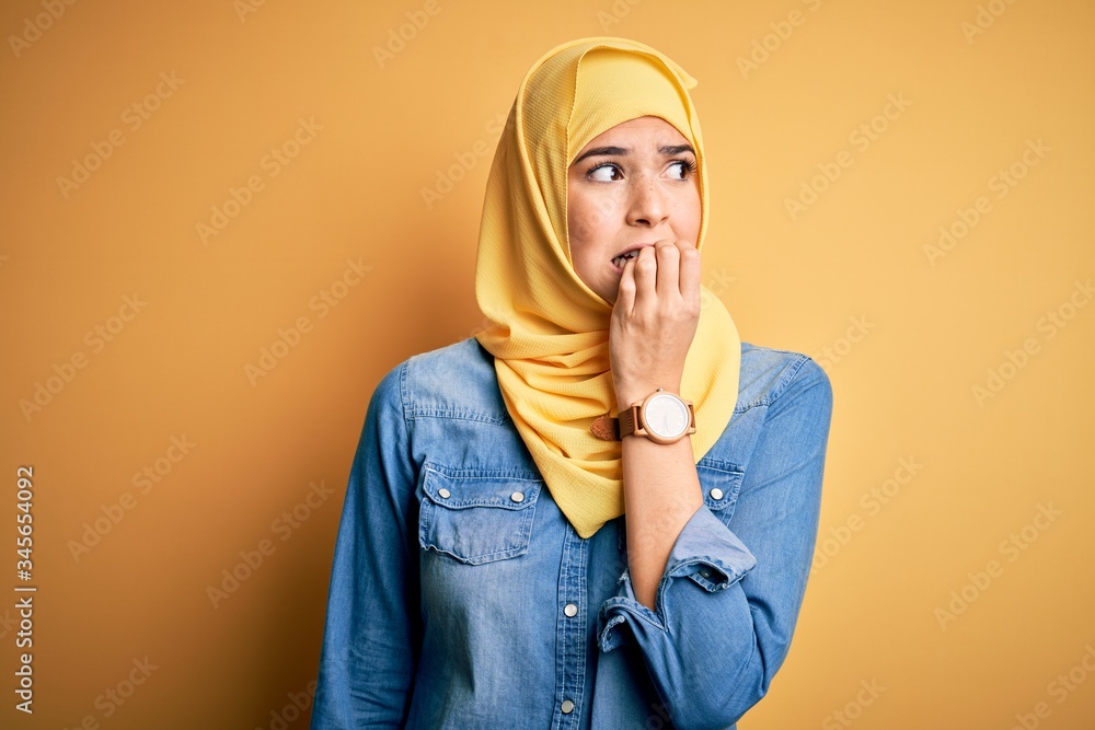 Poster young beautiful girl wearing muslim hijab standing over isolated yellow background looking stressed 