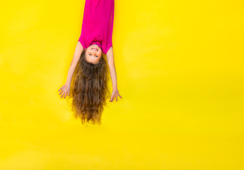 Upside downed little blond girl in bright pink shirt on a yellow background