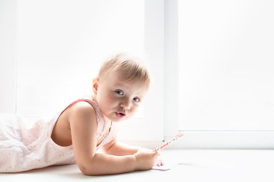 Caucasian baby girl lies and paints on windowsill