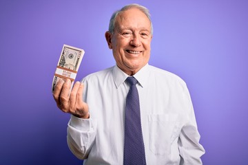 Senior grey haired man holding bunch of fifty dollars banknotes over purple background with a happy...