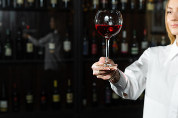 Beautiful blonde young girl sommelier holding up and looking through a glass of wine. Color and bouquet of wine. Close up.