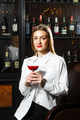 Young beautiful blonde smilling girl sommelier is holding a glass of red wine. Sommelier smelling wine bouquet.