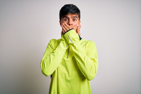 Young handsome sportsman doing sport wearing sportswear over isolated white background shocked covering mouth with hands for mistake. Secret concept.