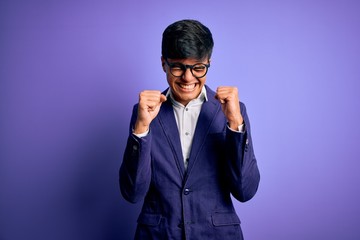 Young handsome business man wearing jacket and glasses over isolated purple background excited for success with arms raised and eyes closed celebrating victory smiling. Winner concept.