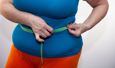 Measure the waist with a centimeter tape. The problem of excess weight. Full belly and folds. Hands of a woman dieting. Losing weight. Weight gain. Place for text.