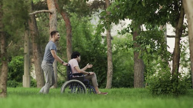 A person helping to a disabled man. Man is taking care of disabled and helping him to relax in the park in his wheelchair.