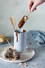 Frozen banana on a stick covered with dark chocolate and crumbs of nuts. A quick, delicious dessert for kids, for a birthday, for a candy bar. Vegan dessert.