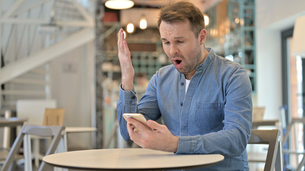 Shocked Casual Man Reacting to Failure on Smartphone in Cafe