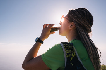 Portrait of young woman drinking some water from a bottle while sitting and resting after trail running