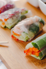 Vertical close up shot of fresh spring rolls with shrimp and vegetables cut in half and different sauces served on a wood plate.
