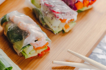 Delicious asian dish. Side view of fresh spring rolls with shrimp and vegetables and different sauces served on a wood plate with chop sticks.