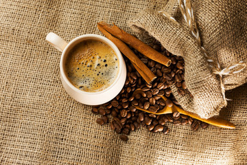Coffee cup with cinnamon sticks and coffee bag on wooden table