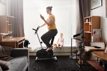 Fototapeta premium Mom on stationary bike communicates over phone
